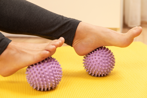 woman massaging feet with pink spiky massage balls