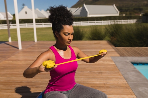 woman working out outdoors while sitting and using resistance bands