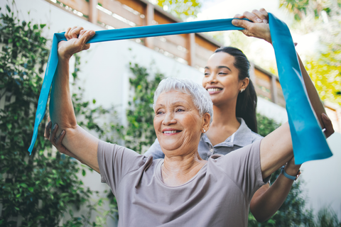 elderly woman using therapy bands with assistance