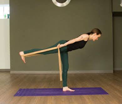woman standing on yoga mat stretching leg with yoga strap