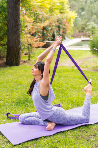 fit woman outdoors stretching leg with yoga strap