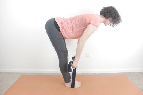 woman on yoga mat stretching and touching toes with yoga strap