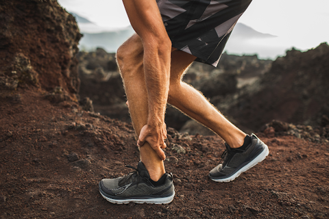 man on tennis shoes massaging a strained foot