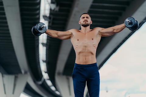 man in gym with arms open and holding weight