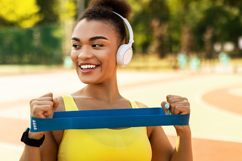 woman outside exercising with headphone ands resistance bands in hand