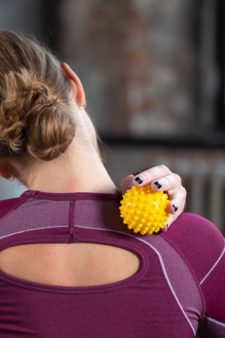 woman massaging neck with yellow spiky massage ball