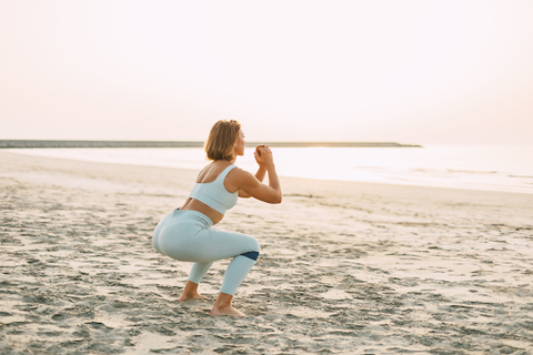 A lady on the beach doing some yoga with a booty band under her knees