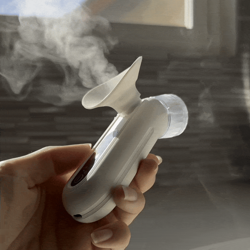 Hand holding a portable steam inhaler releasing vapor.