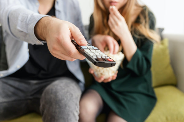 A man and woman eating popcorn and pointing remote at the TV