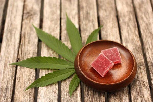 THC+CBD gummies in a dish with a cannabis leaf underneath