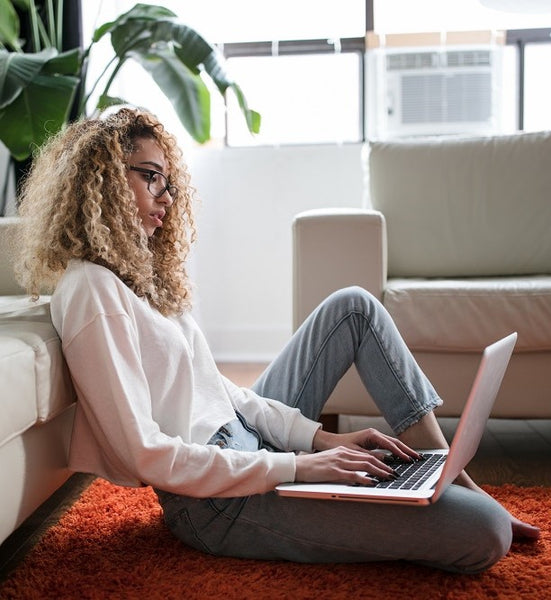 Lady sitting on the floor in a modern apartment using her laptop.