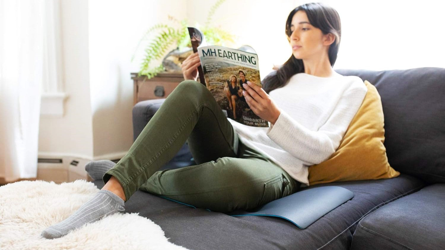 a girl reading on the couch while sitting on a grounding mat