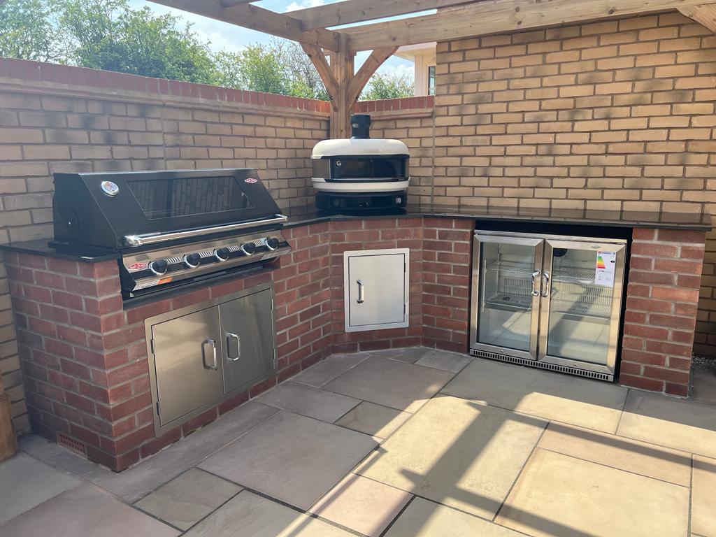 Finished outdoor kitchen equipped with pizza oven, BBQ and double door fridge