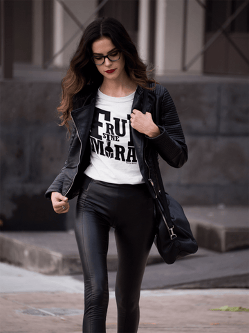 Beautiful young woman in a hurry, with long brown hair, dressed in a leather jacket and black pants: she wears a white t-shirt written in big letters and in black capital letters Frui Sine Mora
