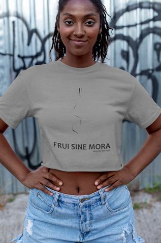 Jeune femme noire portant un t-shirt gris, avec un motif sous forme de lignes noires représentant un demi-casque grec de face. Sous le croquis, inscrit Frui Sine Mora