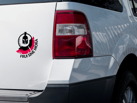 Autocollant posé à l’arrière d’une voiture du logo officiel Frui sine Mora ( représentant un casque grec noir de face avec au dessus une aile noire et une aile rouge plus grande en arc de cercle )