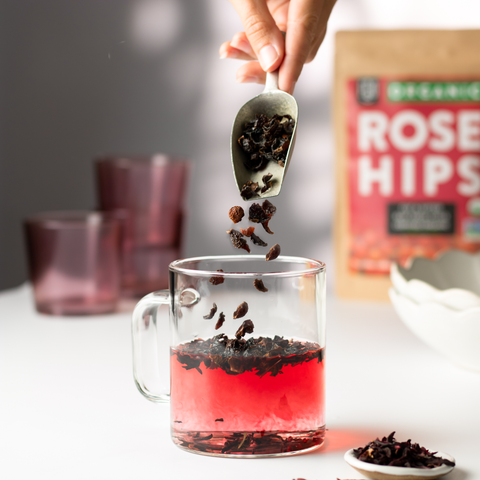 A scoop of dried rosehips dropped into a glass of hot water.