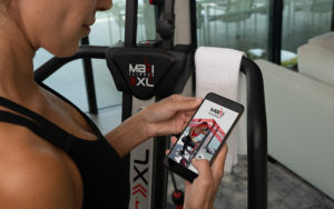 Woman holding a mobile phone showing the MaxiClimber Fitness App that can guide you to a 10 minute workout to start your day strong