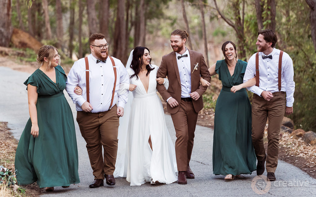 Lauren and Alex walk arm-in-arm with their wedding party; the bridesmaids are dressed in emerald green.