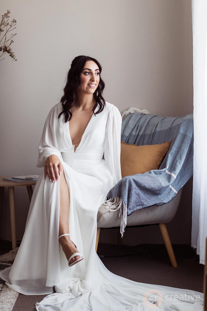 Lauren is gracefully perched on a seat in her bridal suite, dressed in her beautiful bridal gown.