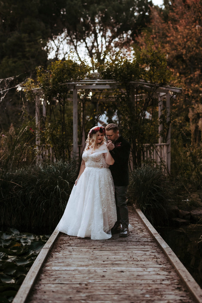 Chantelle and Dave stand side-by-side beneath a gazebo covered in vines of ivy.