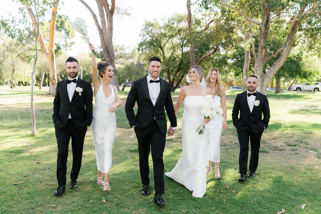 Hannah and Luca stand side by side with their bridal party. Luca and his groomsmen are dressed in elegant black suits, the bridesmaids wear ivory silk dresses.