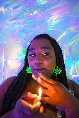 Young woman wearing pot shaped LED earrings while lighting up a joint.