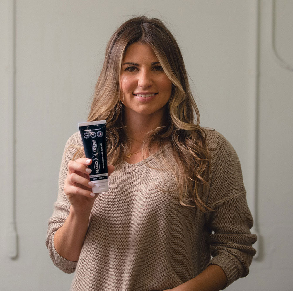 A person holding a tube of Nano-Xtreme dental cream, smiling indoors.