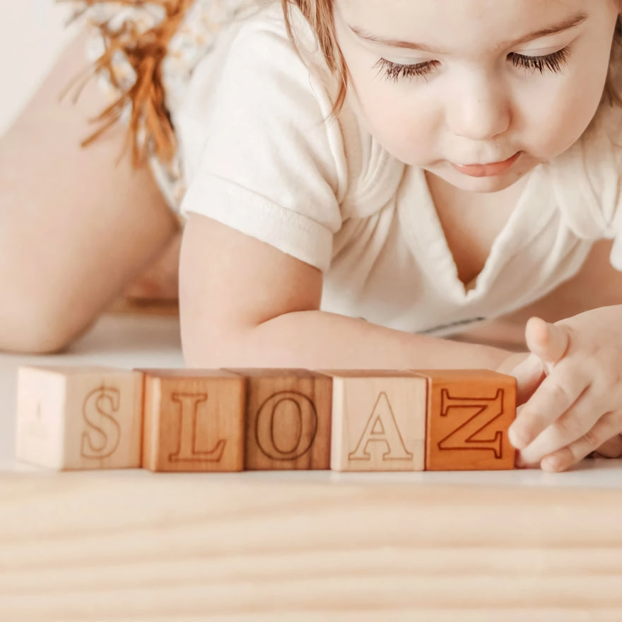 Ein kleines Mädchen ordnet auf dem Boden liegende Alphabetblöcke