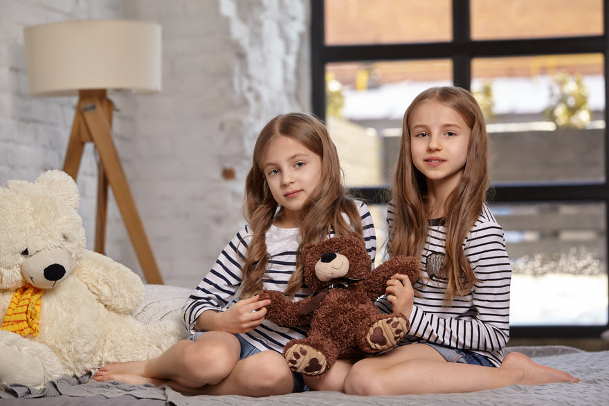 2 Mädchen mit Teddybären sitzen auf dem Bett