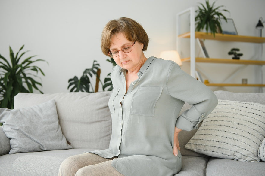 Ältere Frau sitzt auf dem Sofa massiert Rückenschmerzen mit der Hand