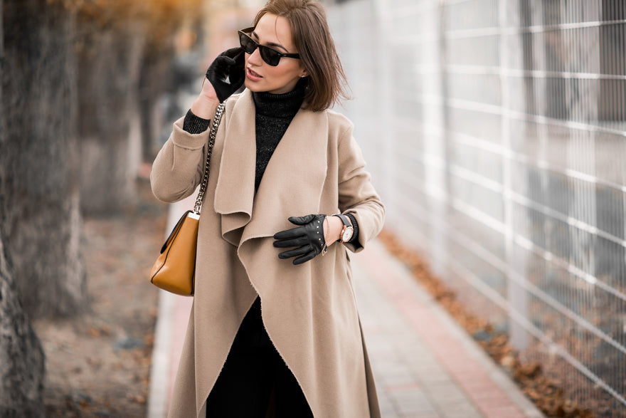 Frau trägt beigen Mantel mit dem Handy und der Brille