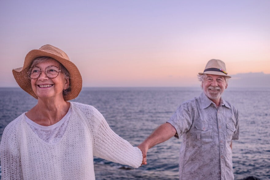 Fröhliches Senioren-Paar mit Hüten genießt Meer im Urlaub