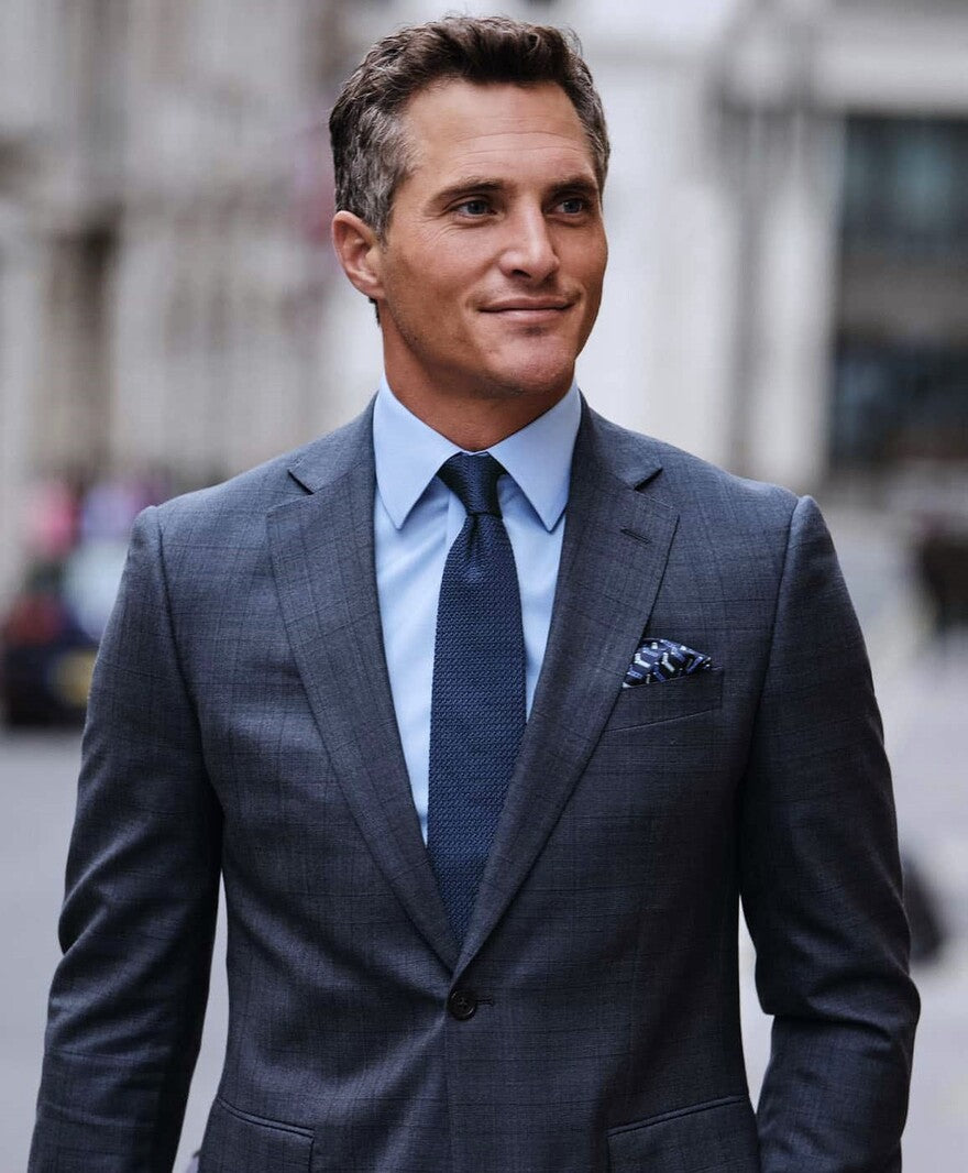 Ein Mann trägt einem grauen Anzug und lächelt
