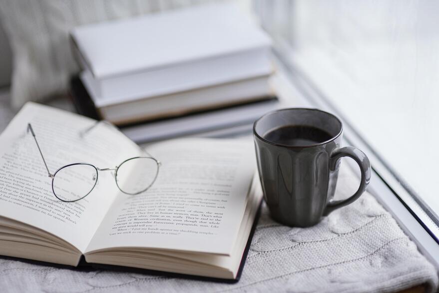 Eine Brille liegt auf dem Buch und Kaffee-Tasse