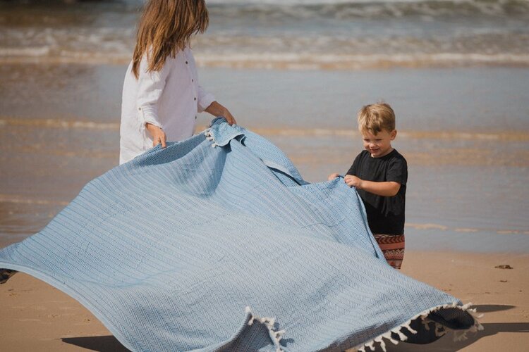 Woman and child spreading an Ozoola family beach blanket on the sand