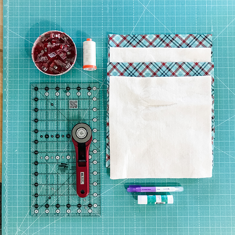 Green cutting mat with ruler, rotary cutter, Clover clips, thread, marking pen, glue, fabric and batting squares