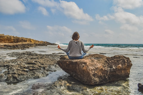 une jeune femme qui médite sur un rocher à la plage