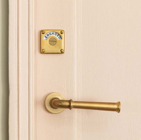 Aged brass lever handles and vacant engaged lock on pink door with green architrave