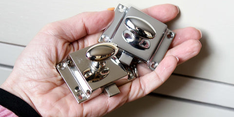 a polished chrome cabinet catch side by side with a polished nickel cabinet catch