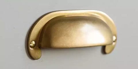 Curved hooded drawer pull made from solid brass with an aged finish on grey drawer