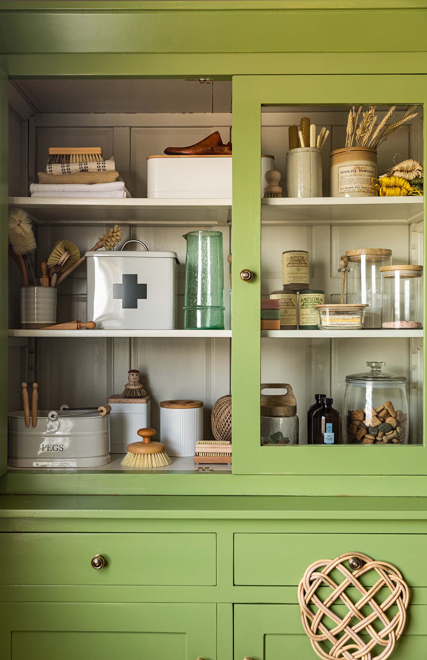 Bright green kitchen dresser with brass knobs and glass doors with laundry storage ideas inside