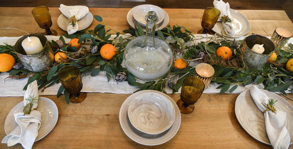 Mixed neutral crockery settings on wooden table with foliage and oranges