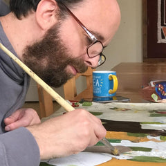 Disabled artist Nick Mair painting. Head quite close to the canvas as he paints, holding the paint brush. Nick has brown hair and beard. He wears glasses.