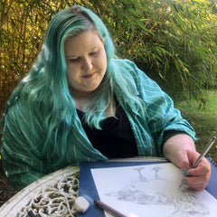 Disabled artist, ella walker in the garden with a sketchpad. Pen in hand, smiling.