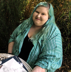 Disabled artist, ella walker in the garden with a sketchpad. Pen in hand, smiling.