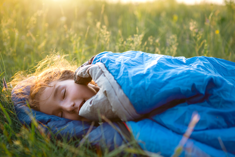 young girl sleeping in grass with a sleeping bag