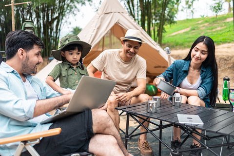 family sitting at table with laptop at campsite