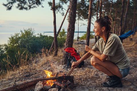 woman in shorts sitting at campsite at campfire