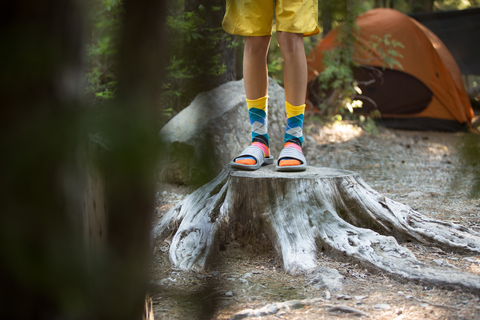 child in socks and flip flops stand on cut tree at campsite